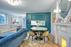 Een moderne keuken met blauwgroene kastjes, een wit marmeren aanrecht en een eethoek met een ronde tafel en stoelen.