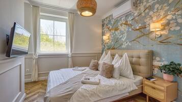 Ein Schlafzimmer mit einem Bett, einem Fernseher, einem Fenster, einer Wandlampe und einem Nachttisch mit einer Pflanze.