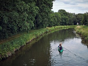 Een smalle waterweg, omzoomd door weelderige begroeiing, met een klein gebouw in de verte.