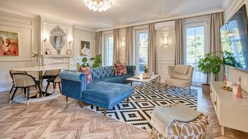 Un salon spacieux avec un canapé bleu, un coin repas doté d’une table ronde et une grande fenêtre laissant entrer la lumière naturelle.