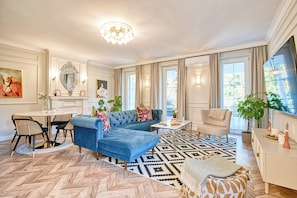 A spacious living room with a blue sectional sofa, a patterned rug, and a dining area with a table and chairs.