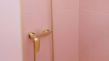 Chuveiro com chuveiro e mangueira dourados em frente a uma parede de azulejos cor-de-rosa.