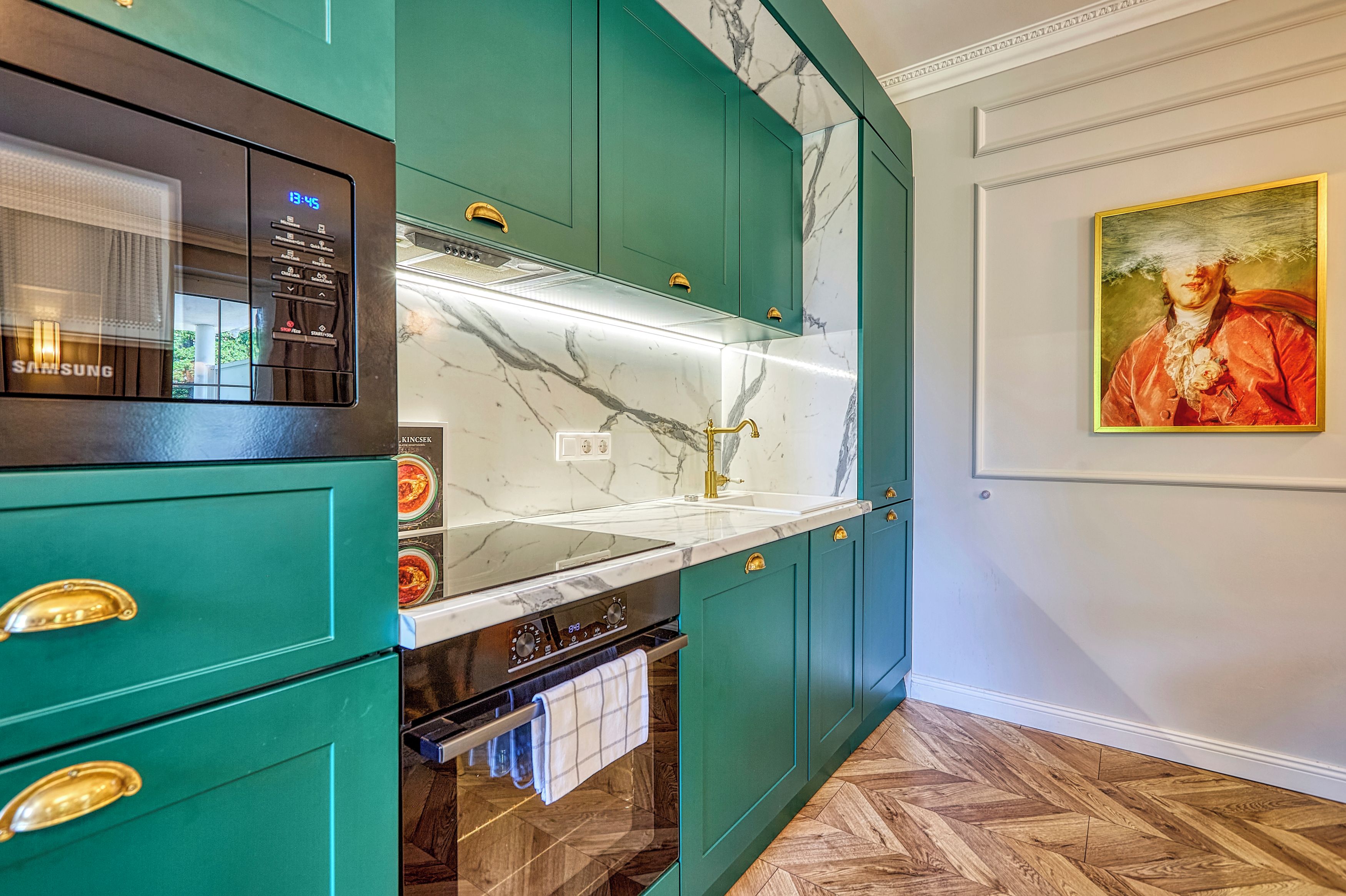 Una cocina con armarios verde azulado, encimera de mármol y un cuadro en la pared.