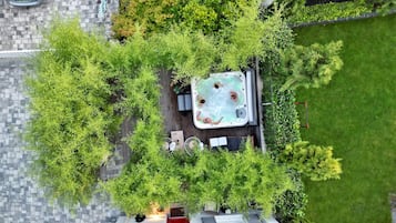 Vista aérea de un jardín en la azotea con un jacuzzi, rodeado de exuberante vegetación y un camino pavimentado.