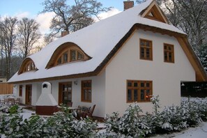 A snow-covered house with a thatched roof, wooden windows, and a chimney. - Holiday home Amber seeker (Sellin)