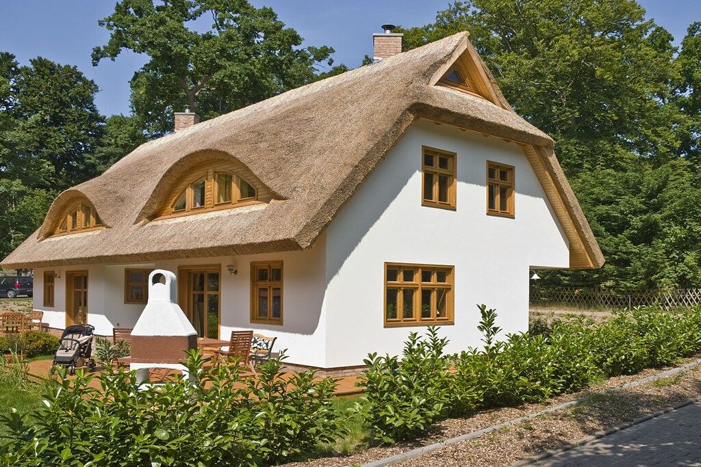 Una casa blanca con techo de paja y ventanas de madera.