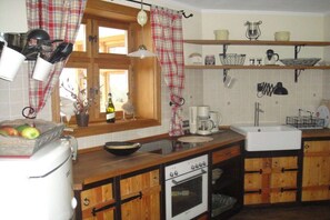 A kitchen with wooden cabinets, a built-in oven, a sink, and a window with curtains. - Holiday home Amber seeker (Sellin)