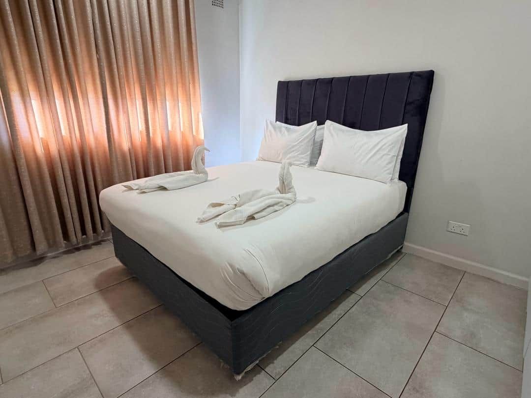 A bed with a dark headboard, white bedding, and a pair of white towels.