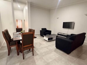 Un salon moderne comprenant une table à manger, des chaises, un canapé et un téléviseur à écran plat fixé au mur.