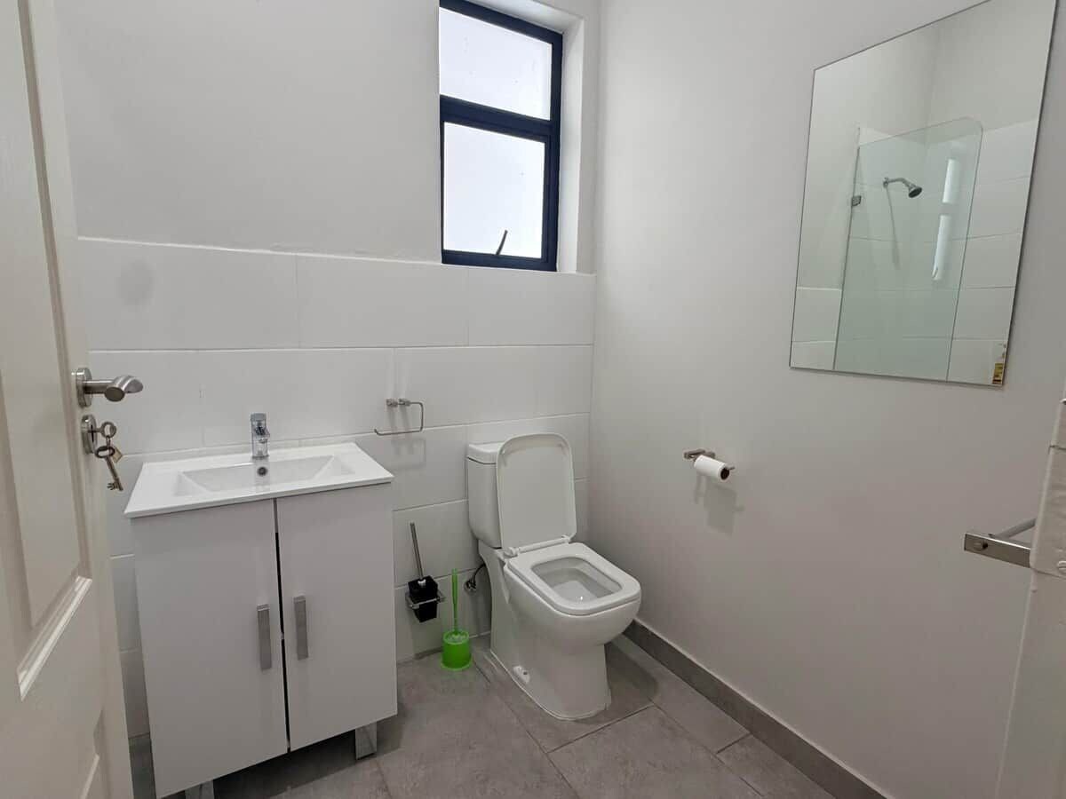 A small bathroom with a toilet, a sink, a window, and a mirror.