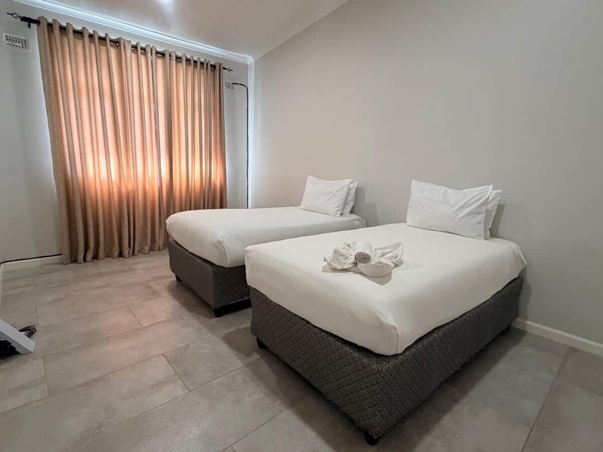 A hotel room with two beds, a large window with curtains, and a tiled floor.