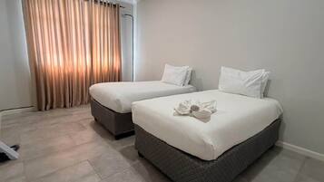 A hotel room with two beds, a large window with curtains, and a tiled floor.