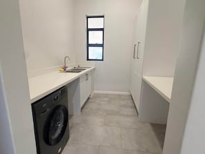 A laundry room with a washing machine, a sink, and a window. - Dreams Apartment 115 (Victoria Falls)