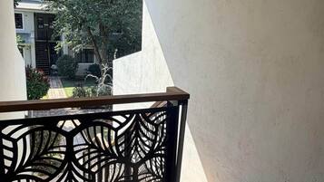 A balcony with a geometric metal railing, a tiled floor, and a view of a residential area with trees and a building.