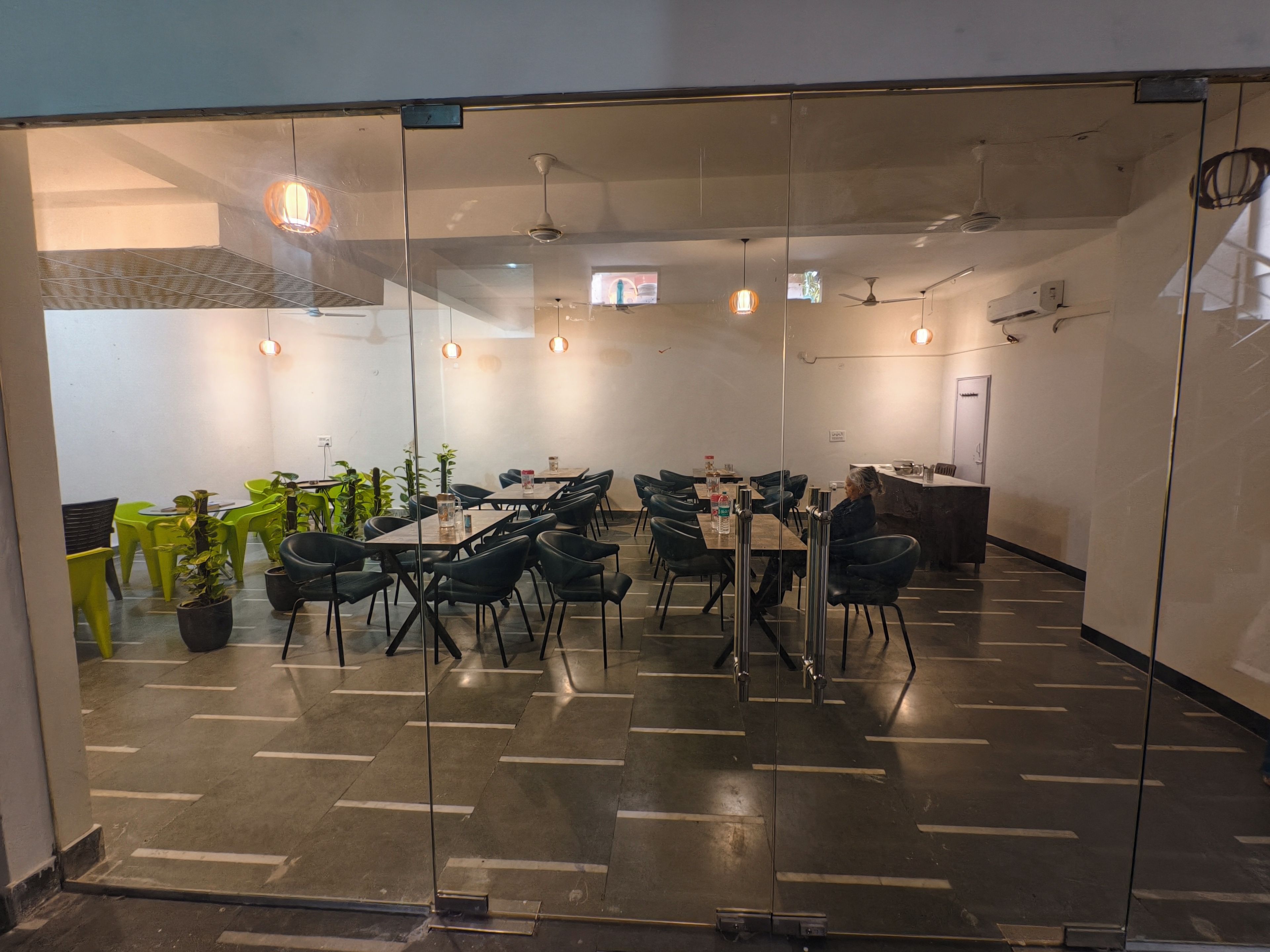 A conference room with glass walls, multiple tables, chairs, ceiling fans, and hanging pendant lights.