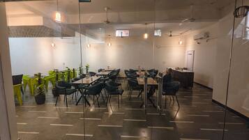 A conference room with glass walls, multiple tables, chairs, ceiling fans, and hanging pendant lights.