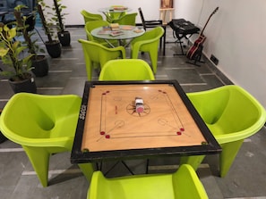 A room with a foosball table surrounded by green chairs, a guitar, and potted plants. - hotel roomin (Noida)
