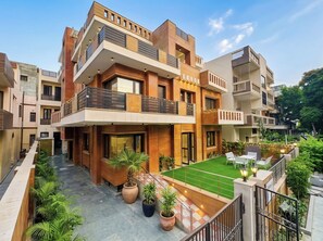 Un edificio residencial moderno de varios pisos con patio, mobiliario exterior y plantas en macetas.