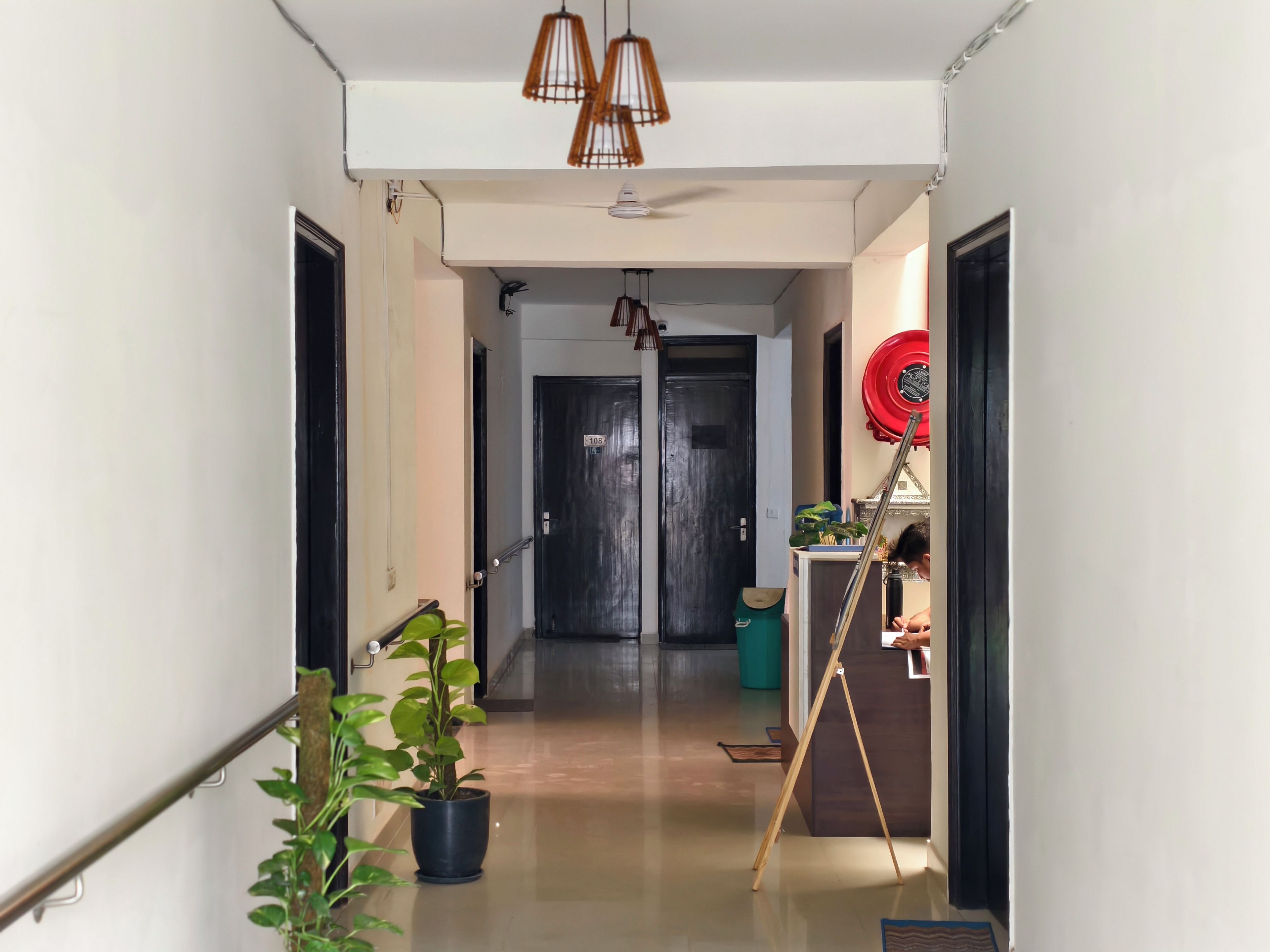 A hallway with a potted plant, a door with a number sign, and a red circular object on the wall.