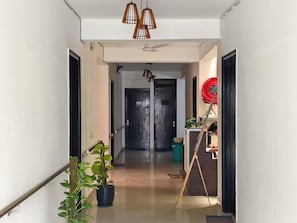 Un passadís amb una planta en test, una porta amb el símbol de número i un objecte circular vermell a la paret.