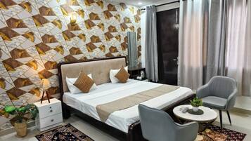 Una habitación de hotel moderna con una cama grande, dos sillones, una mesita y un detalle decorativo en la pared.