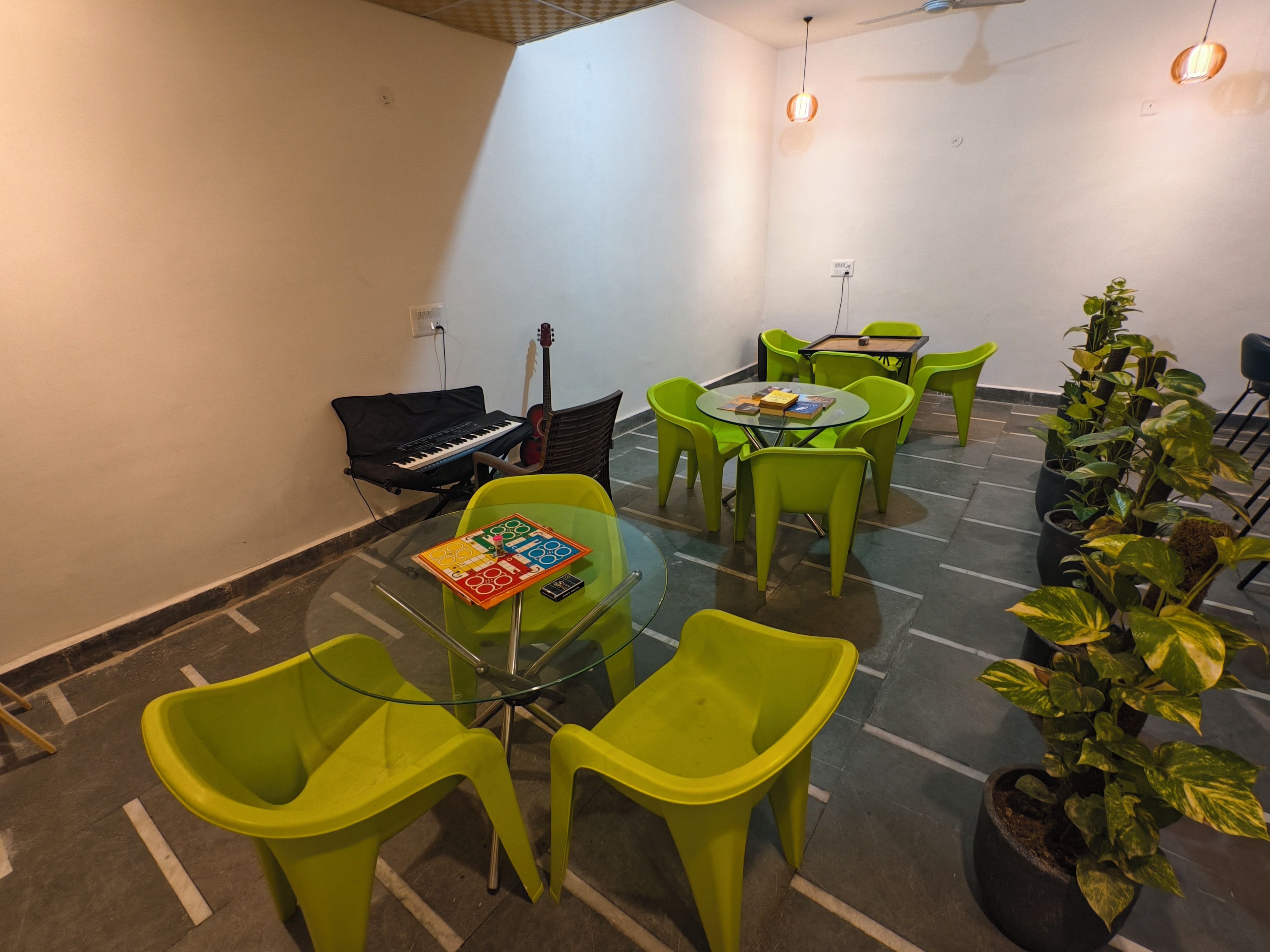 Una habitación con una mesa de vidrio rodeada de sillas verdes, un teclado, una guitarra y una planta en maceta.