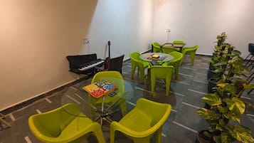 Una habitación con una mesa de vidrio rodeada de sillas verdes, un teclado, una guitarra y una planta en maceta.