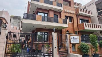 Un edificio de varios pisos con entrada protegida por un portón, un letrero y macetas con plantas.