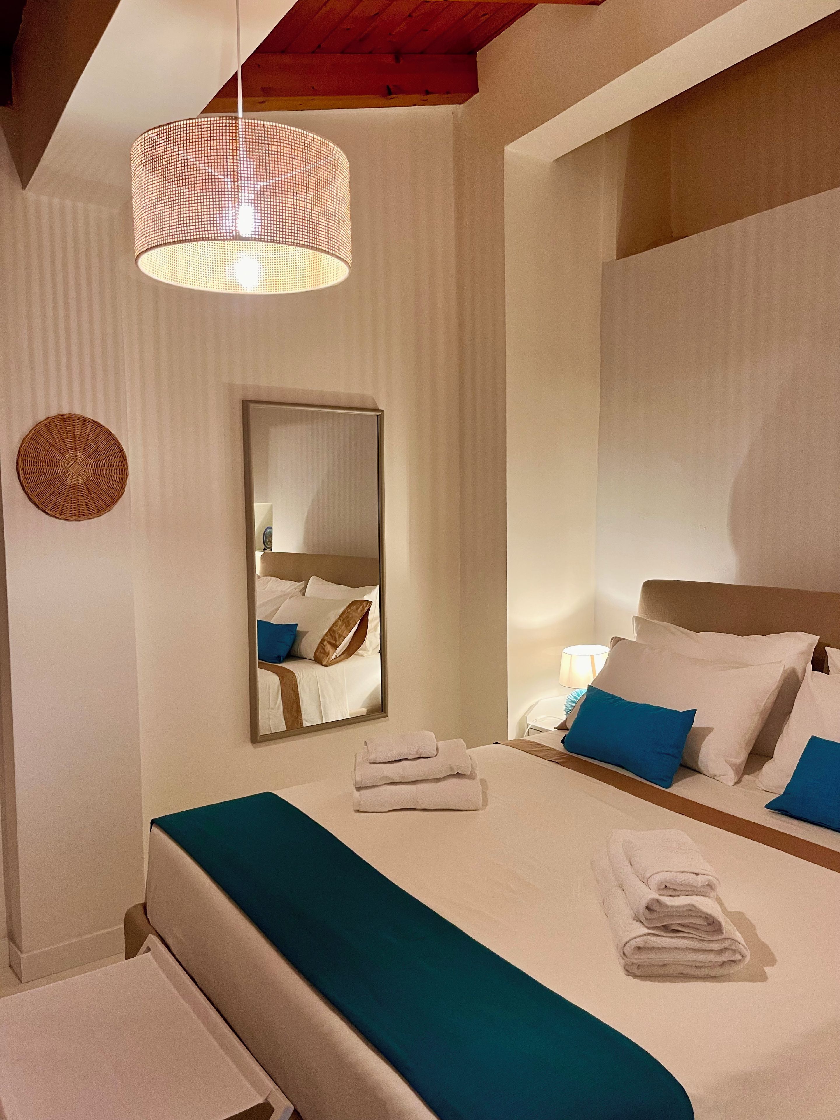 Una camera d'albergo con un letto, uno specchio, un lampadario a sospensione e un oggetto circolare fissato al muro.