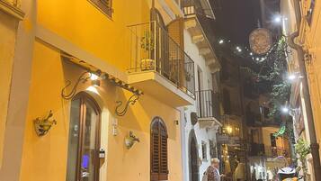 Una stretta via acciottolata con un edificio giallo che presenta un balcone con ringhiera, una porta e una finestra con persiane.