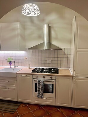 Eine Küche mit weißen Schränken, einem Gasherd, einem Backofen und einer Edelstahl-Dunstabzugshaube.
