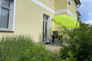 A building with a yellow facade, a door, and a patio area with a table and chairs. - Fischerweg - Villa Angelika (Seebad Bansin)