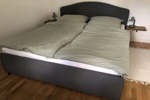 Een bed met een donker hoofdbord, twee nachtkastjes met lampen en een houten vloer.