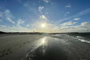 Ein Strand mit blauem Himmel und Sonnenlicht, das auf dem feuchten Sand glitzert.
