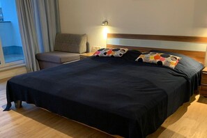 A hotel room with a large bed, a nightstand, a lamp, a sofa, and a window with curtains. - Holiday apartment Yachthafenresidenz 319437 (Kühlungsborn)