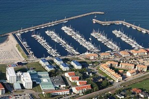 Eine Vogelperspektive auf eine Marina mit zahlreichen vertäuten Booten, umgeben von Wohngebäuden und einem Hotel mit markantem, grüner Dach.