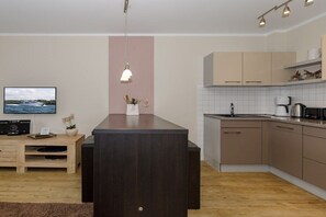 A modern kitchen with a central island, wooden cabinets, and a flat-screen TV on the wall. - Holiday apartment holiday dreams by the sea 319538 (Kühlungsborn)