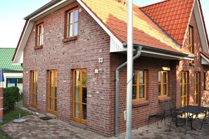 A two-story brick building with a red-tiled roof, numbered 33, featuring large windows and a patio area with outdoor seating. - Holiday home with 2 bedrooms (Kaltenhof (Insel Poel))