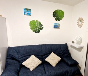 Ein Zimmer mit einem dunkelblauen Sofa, zwei Zierkissen und drei an der Wand hängenden Kunstwerken, darunter zwei große grüne Blätter und ein kleines Landschaftsbild.