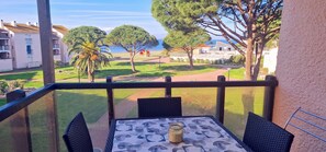 En balkon med bord og stole, der kigger ud over en græsplæne med træer og et fjerntliggende bybillede.
