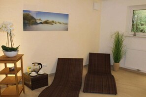 A room with two reclining chairs, a small table with a plant, a picture on the wall, and a window with a view of greenery. - Holiday home in Nebel/Süddorf with sauna (Nebel\/Süddorf)