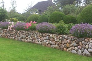 A stone retaining wall with a variety of flowering plants and neatly trimmed bushes. - Holiday home in Nebel/Süddorf with sauna (Nebel\/Süddorf)