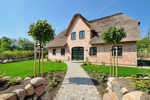 Ein Haus mit Backsteinfassade, einem Strohdach, einem gepflasterten Einfahrt und einem gepflegten Rasen.