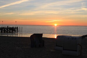 Ein Strandbild mit Sonnenuntergang, einem Steg und Liegestühlen.