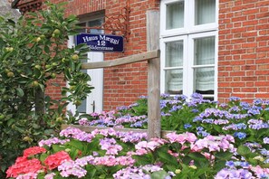 Ein Backsteinhaus mit einem Schild, auf dem 'Haus Mäggi 12 Süderstraße' steht, und einem Garten mit Hortensienblüten.