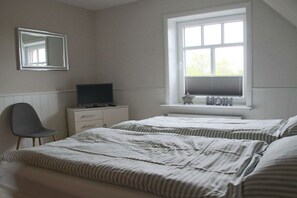 Ein Schlafzimmer mit zwei Betten, einem Fernseher auf einer Kommode, einem Sessel und einem Fenster mit Jalousien.