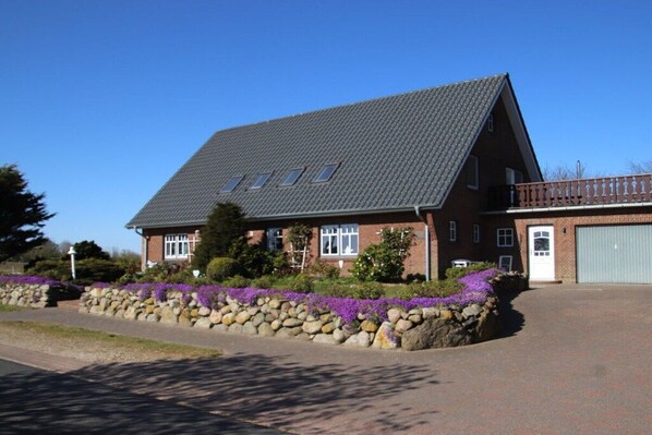 Ein zweistöckiges Haus mit geneigtem Dach, einer Garage und einer Steinmauer mit violetten Blumen.