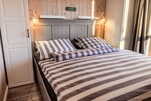 A bed with striped bedding and two pillows, a wooden wall with a sign, and a door. - Holiday home in the North Sea with 2 bedrooms (Wesselburenerkoog)