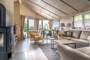 A cozy living room with a fireplace, wooden walls, a sofa, a coffee table, and a dining area with a table and chairs. - Holiday home in the North Sea with 2 bedrooms (Wesselburenerkoog)