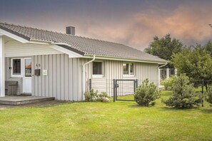 Yhden kerroksen talo, jonka ulkoseinät ovat harmaat, siinä on kuisti ja aidattu piha, jossa on pieniä puita.